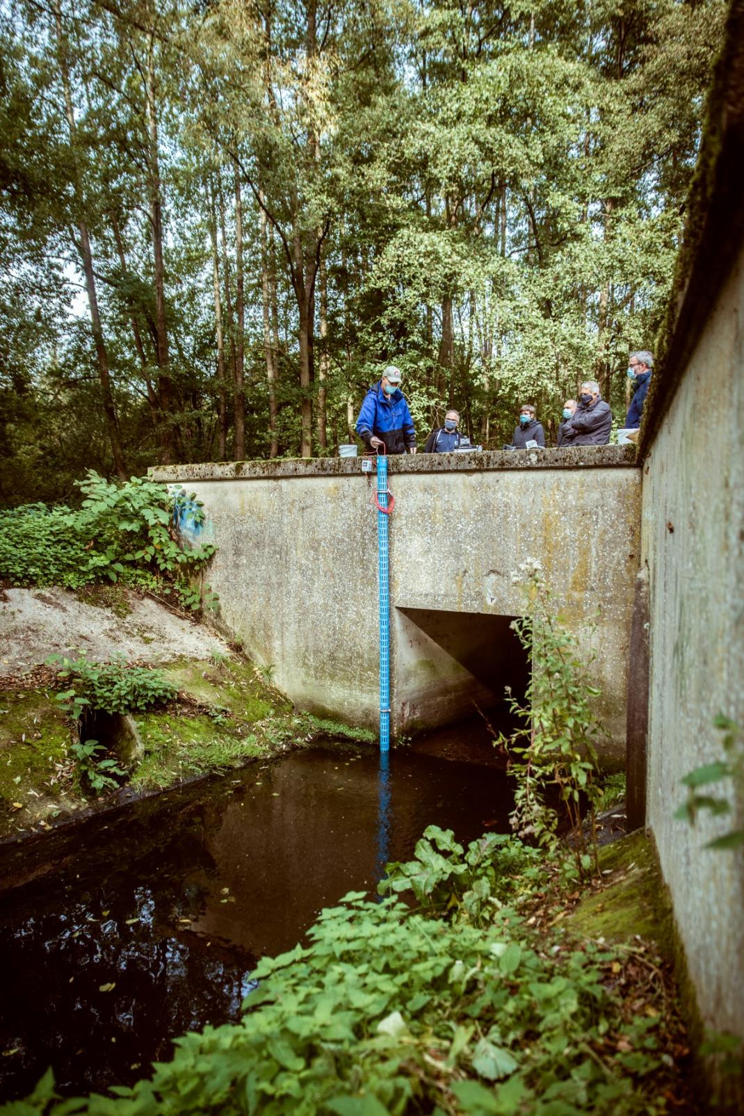 Groep mensen hanteert meetinstrument aan een beek