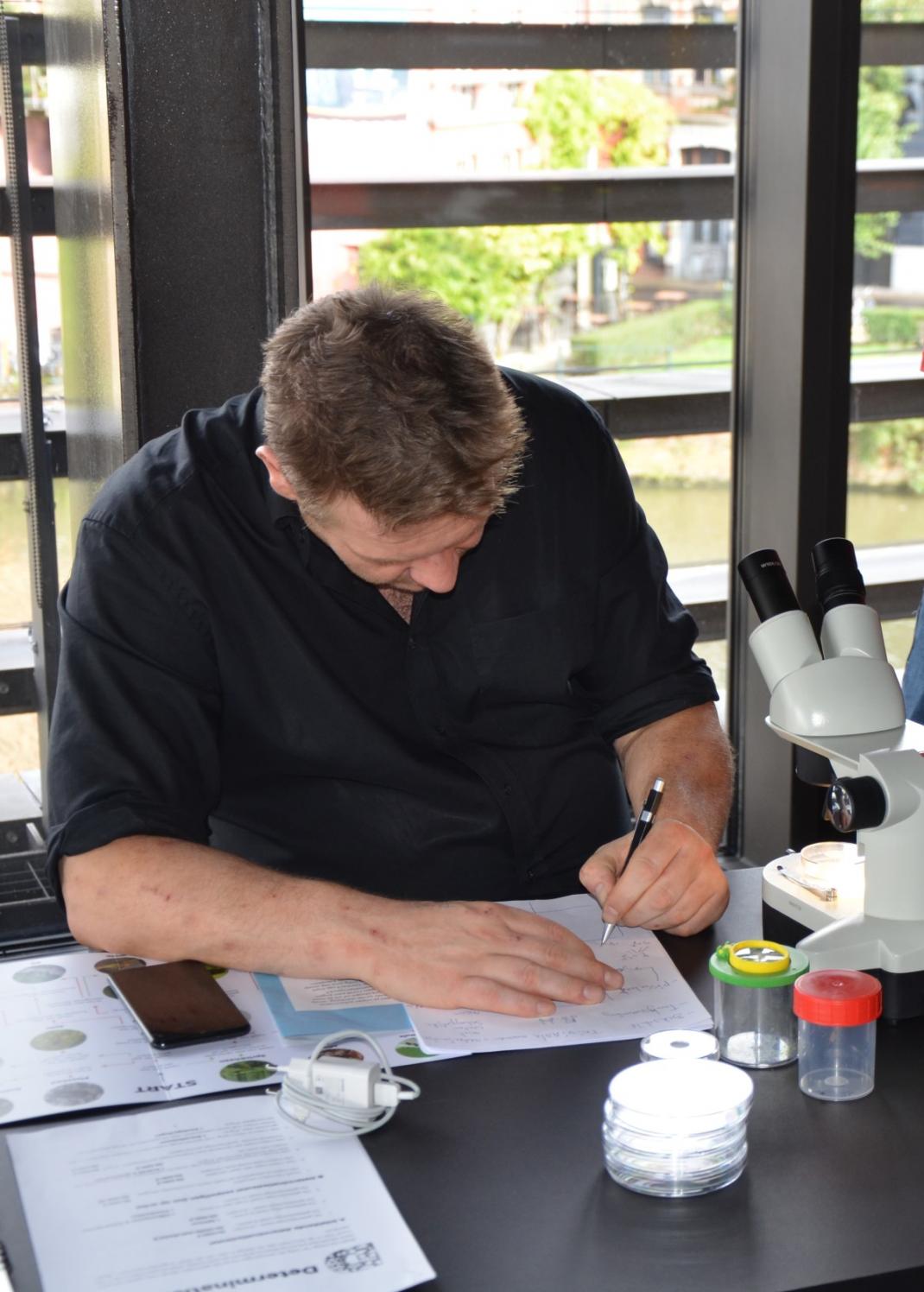 Burgerwetenschapper onderzoekt insect met determinatiekaart en microscoop.